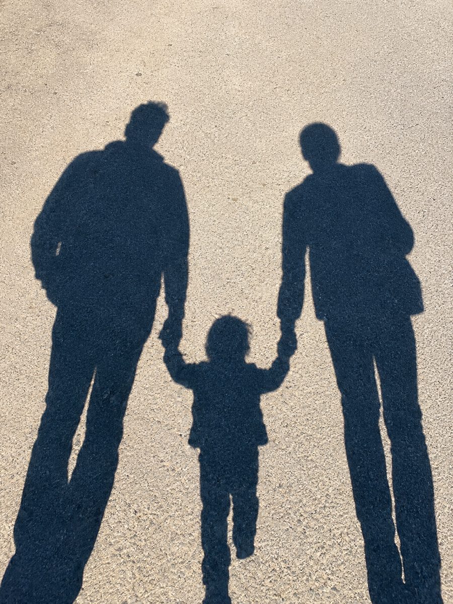 Ombres de deux adultes marchant sur le sable en tenant par la main un jeune enfant placé entre eux.